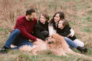 Hampshire Family Photographer - Family sat in the grass looking at each other with their golden retriever dog