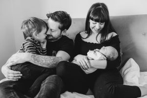 Newborn Family photographer in Hampshire - Black and white photo of young family all snuggling together on the bed with new baby